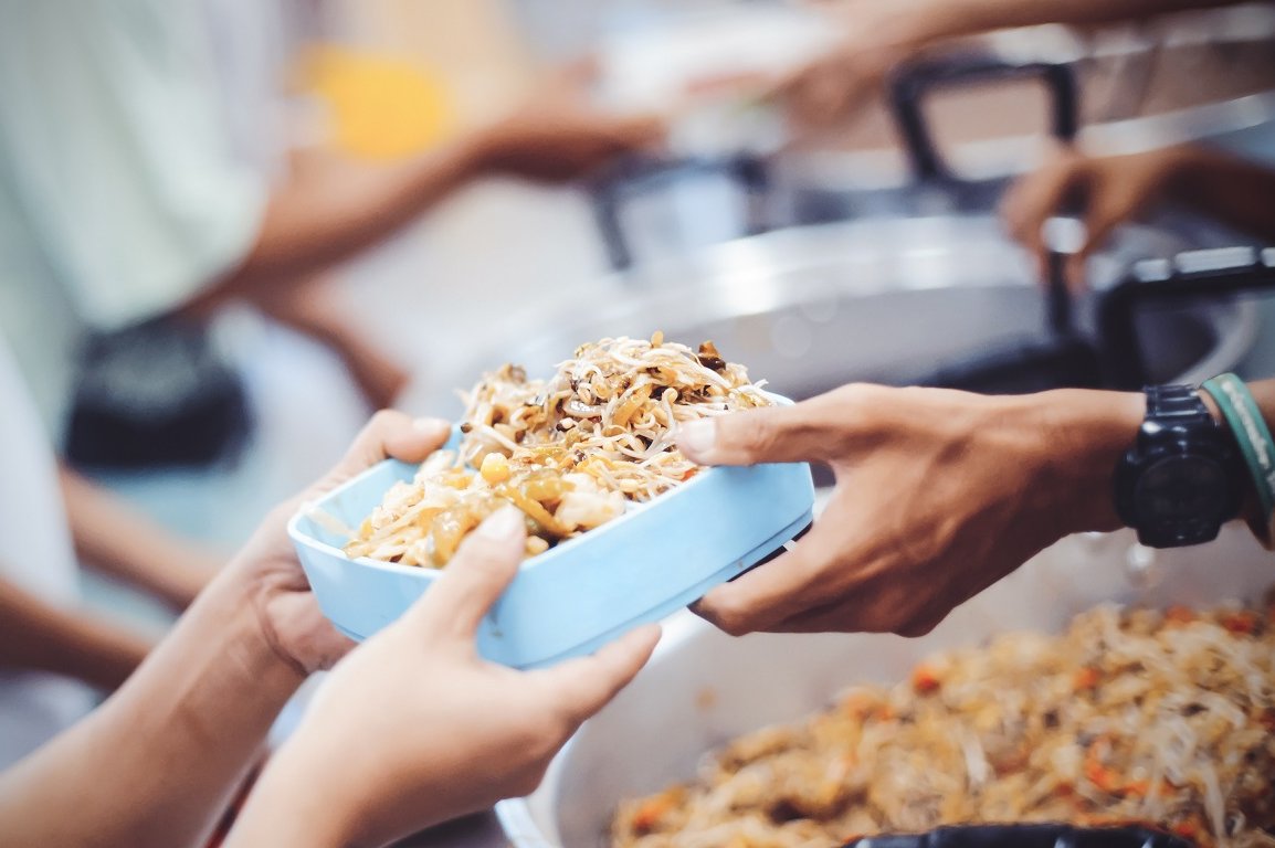 Eine Hand reicht einer Person eine Schale mit Essen.