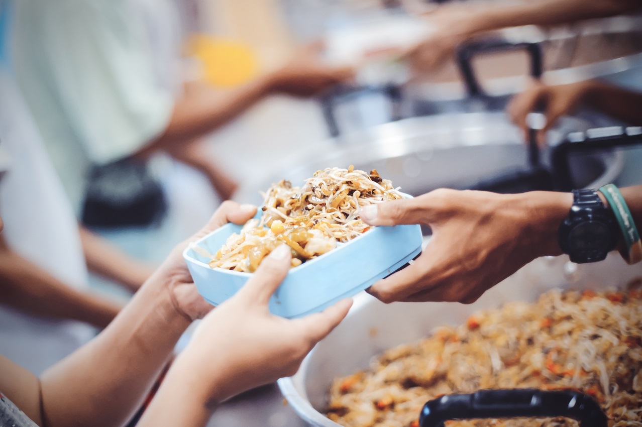 Eine Hand reicht einer Person eine Schale mit Essen.