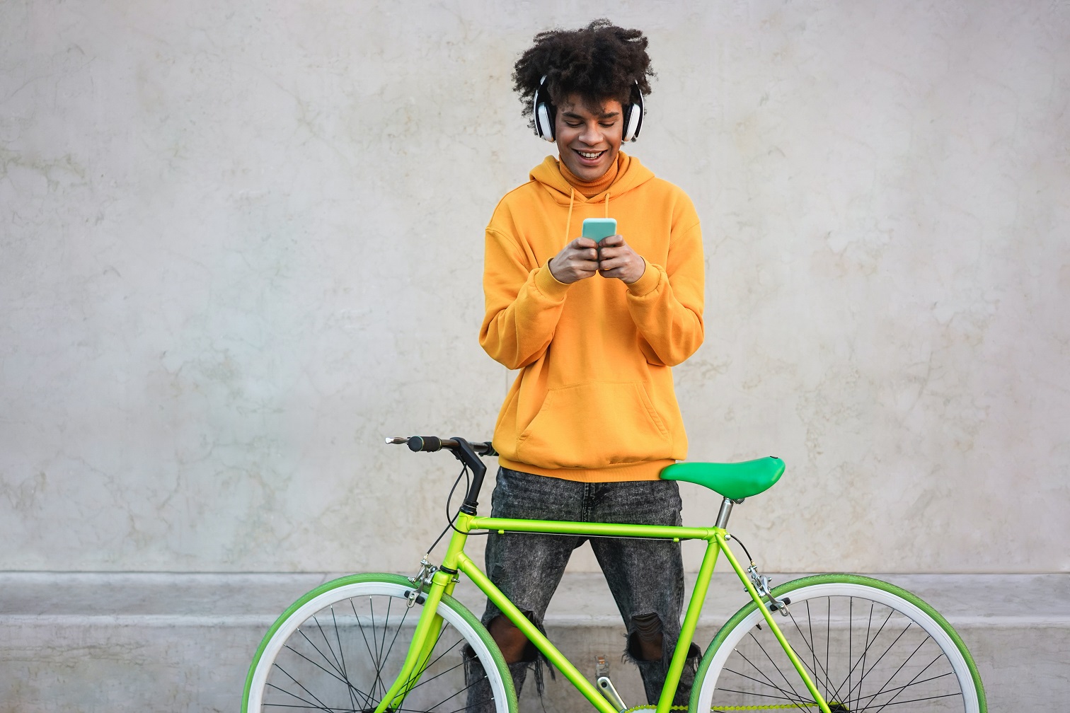 Junger Mann hinter einem grünen Fahrrad schaut aufs Handy.