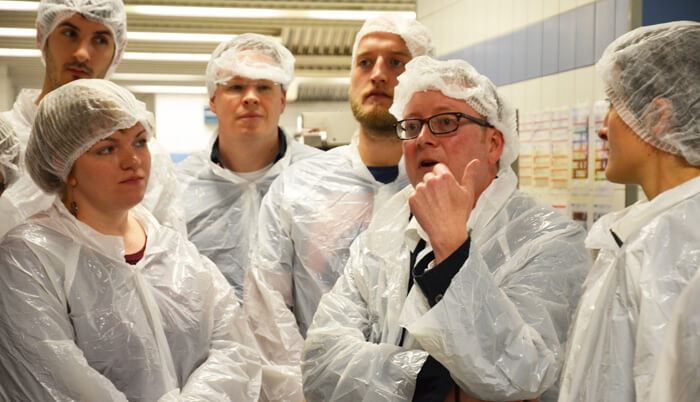 Rundgang-Teilnehmer in Plastikschutzmänteln.