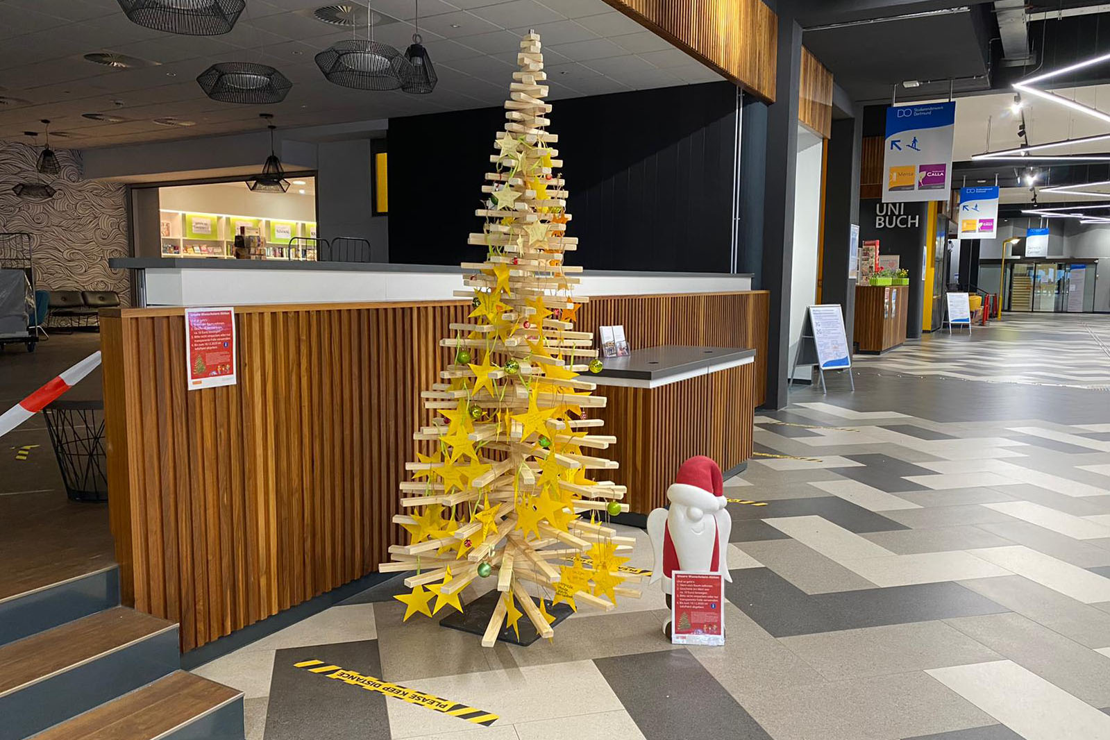 Ein Weihnachstbaum aus Holz mit Kinderwünschen steht im Mensa-Foyer