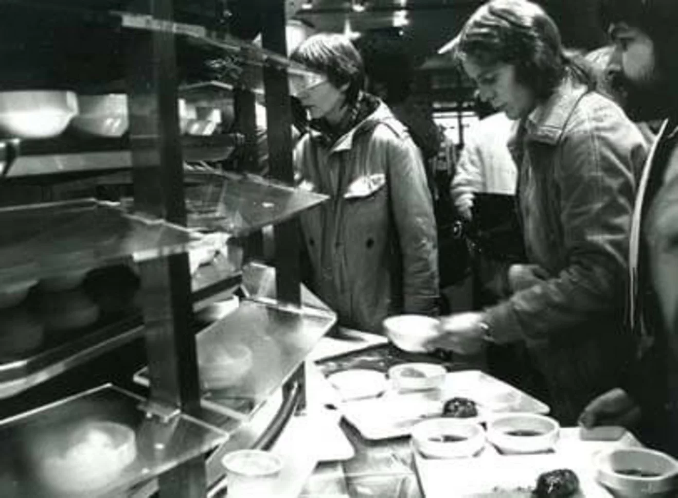 Schwarz-weiß Foto von Studierenden, die sich an einem Essensrondell ihre Mahlzeit aussuchen